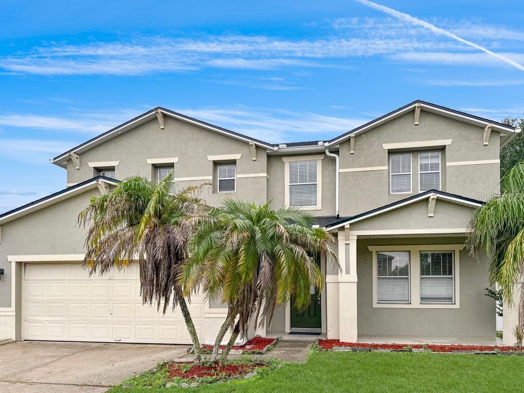 A two-story suburban house with a beige stucco exterior, a garage, and palm trees — 2024 BEARING LANE, KISSIMMEE, FL