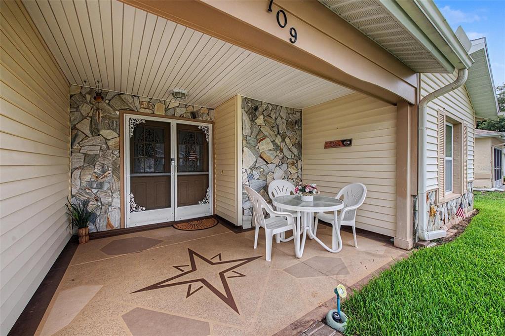A covered front porch features a decorative concrete floor, stone accents, and a small bistro set — 4709 PORTLAND MANOR DRIVE, NEW PORT RICHEY, FL