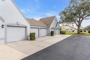 A row of white garage doors sits beside a paved driveway near a large tree — 6807 STONE RIVER ROAD UNIT 202, BRADENTON, FL
