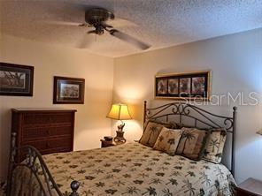 A bedroom features a metal bed frame, a wooden dresser, and a ceiling fan — 6807 STONE RIVER ROAD UNIT 202, BRADENTON, FL