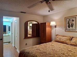 A bedroom features a bed with patterned bedding, a wooden armoire, and an attached bathroom — 6807 STONE RIVER ROAD UNIT 202, BRADENTON, FL