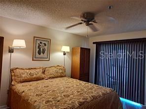 A bedroom features a bed with patterned bedding, two wall-mounted lamps, and vertical window blinds — 6807 STONE RIVER ROAD UNIT 202, BRADENTON, FL
