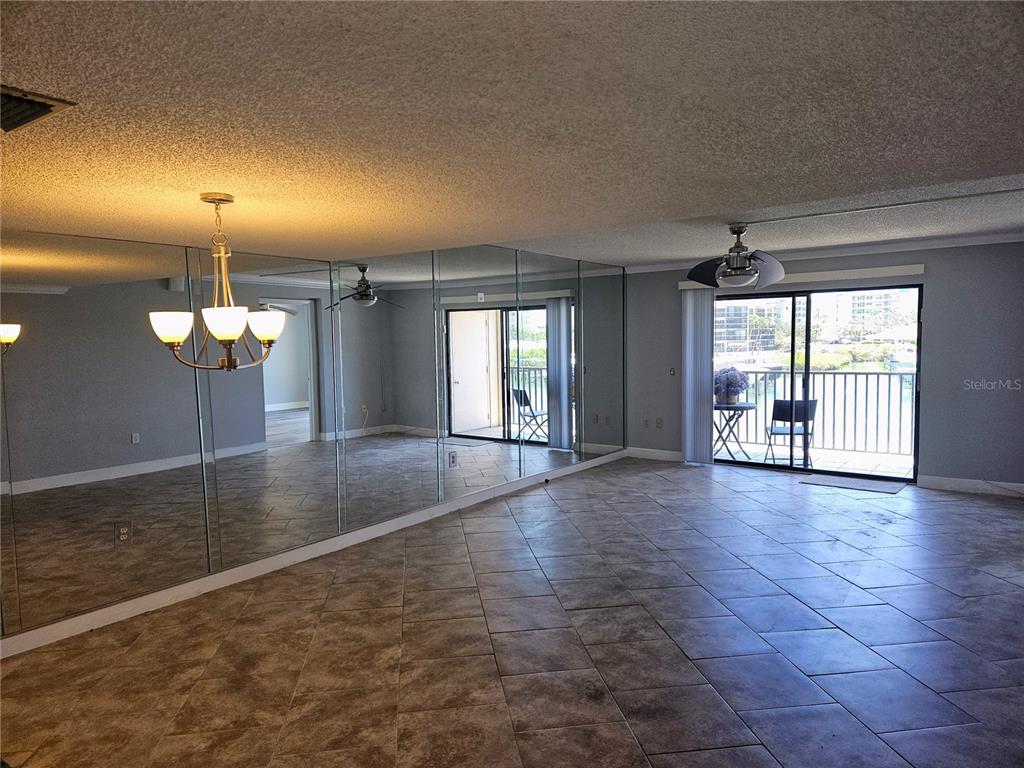 A living room with tiled floors, a mirrored wall, and a sliding door to a balcony — 7600 SUN ISLAND DRIVE S UNIT 204, SOUTH PASADENA, FL