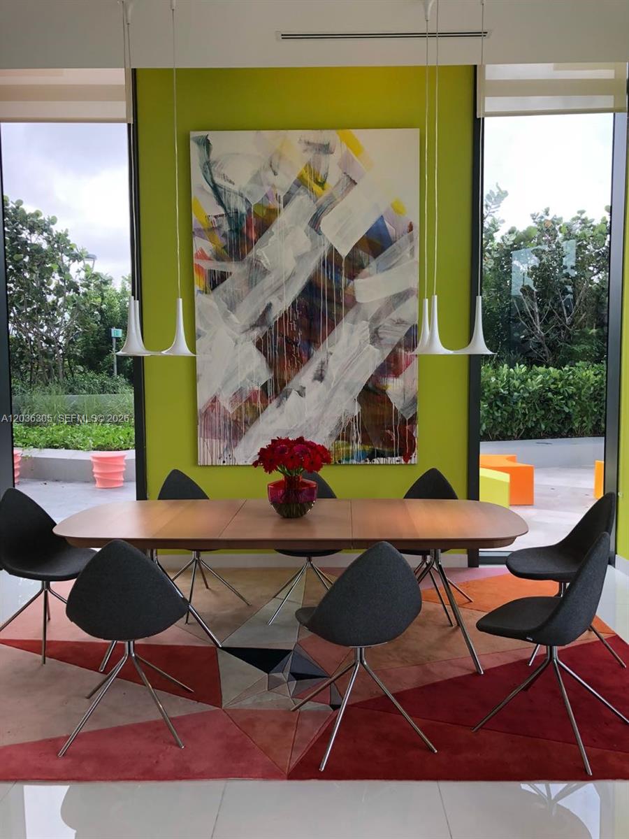 A dining room features a wooden table, grey chairs, a colorful rug, and abstract art — MIAMI, FL