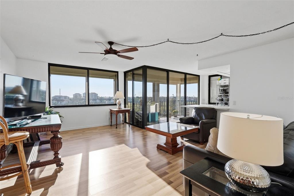 A living room features light wood flooring, a ceiling fan, and a glass-enclosed balcony — 6269 PALMA DEL MAR BOULEVARD S UNIT 608, ST PETERSBURG, FL