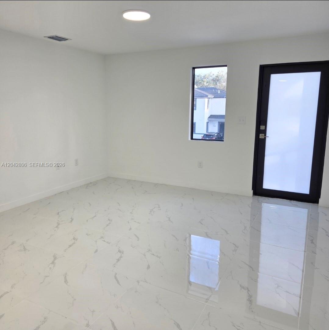 A minimalist room features white walls, glossy marble-patterned tile flooring, a window, and a door — 2729 NW 44 St # 2729, Miami FL 33142, MIAMI, FL