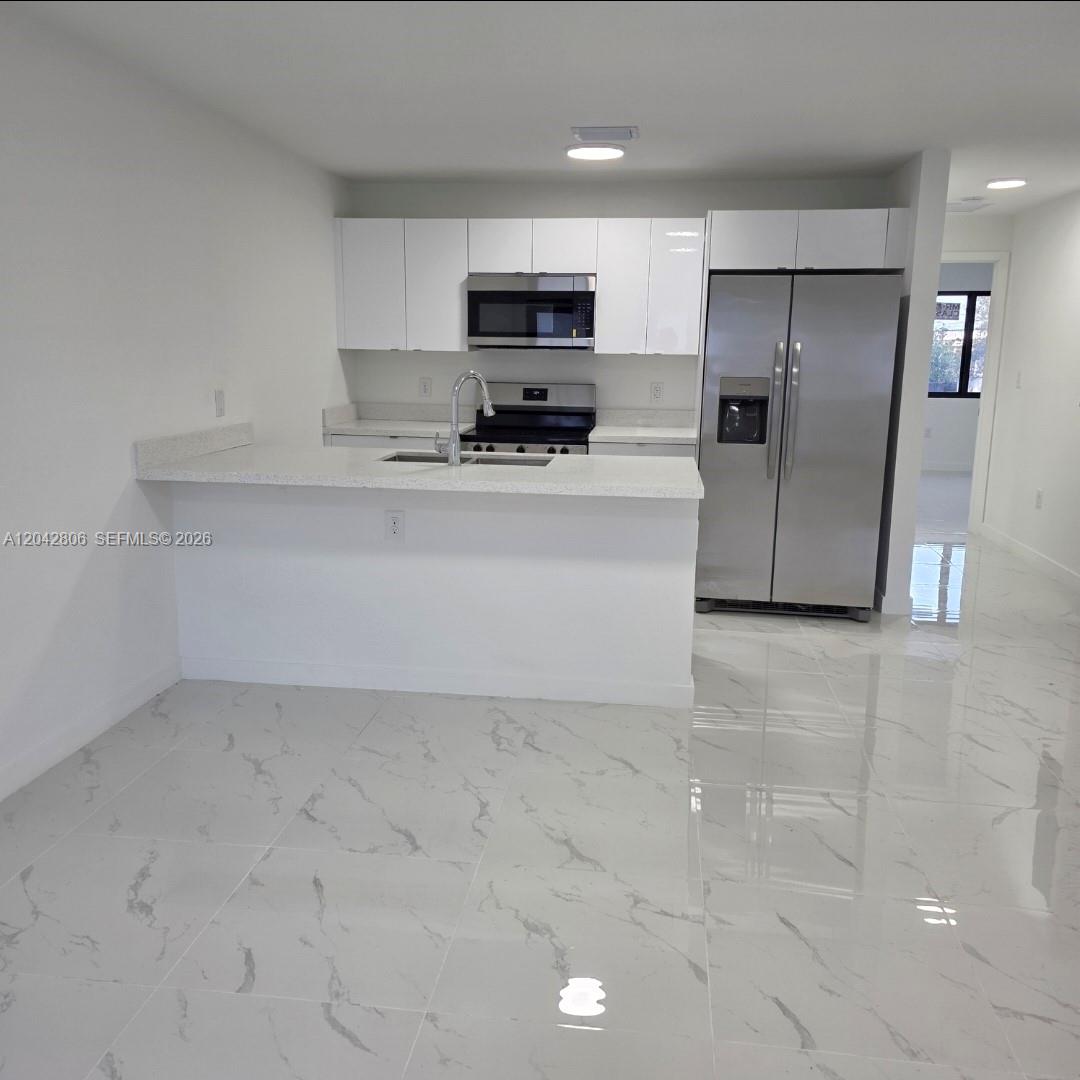 A modern kitchen features white cabinets, stainless steel appliances, and white marble-patterned tile flooring — 2729 NW 44 St # 2729, Miami FL 33142, MIAMI, FL