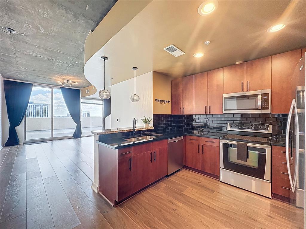 A kitchen with wood cabinets, black tile backsplash, and stainless steel appliances opens to a balcony — 155 S COURT AVENUE UNIT 1013, ORLANDO, FL