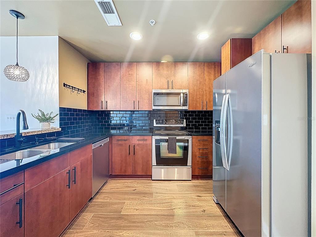 A kitchen features wood cabinets, stainless steel appliances, black subway tile backsplash, and dark countertops — 155 S COURT AVENUE UNIT 1013, ORLANDO, FL