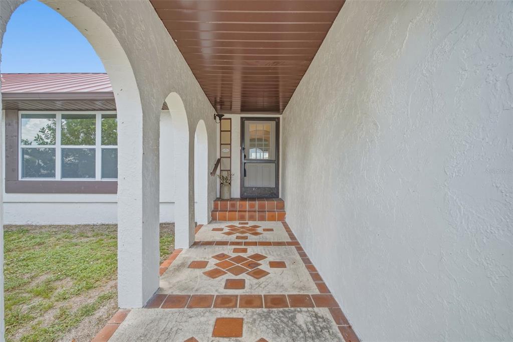 A covered entryway features arched columns, a tiled floor with decorative insets, and a screen door — 235 TAIT TERRACE SE, PORT CHARLOTTE, FL