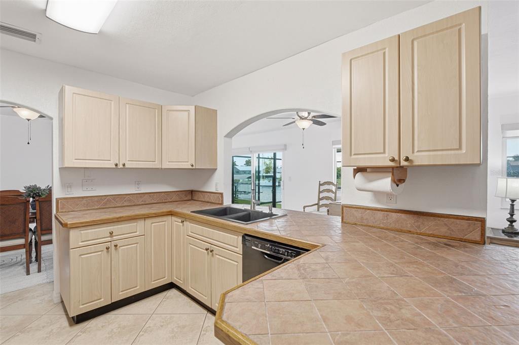 A kitchen with light wood cabinets, tiled countertops, and a view through an arched opening — 235 TAIT TERRACE SE, PORT CHARLOTTE, FL
