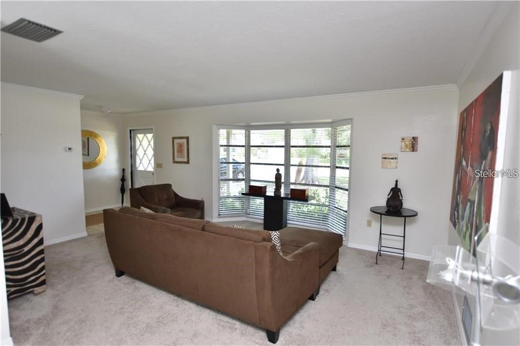 A living room features a brown sectional sofa, a bay window, and neutral carpeting — 3926 CALLIANDRA DRIVE, SARASOTA, FL