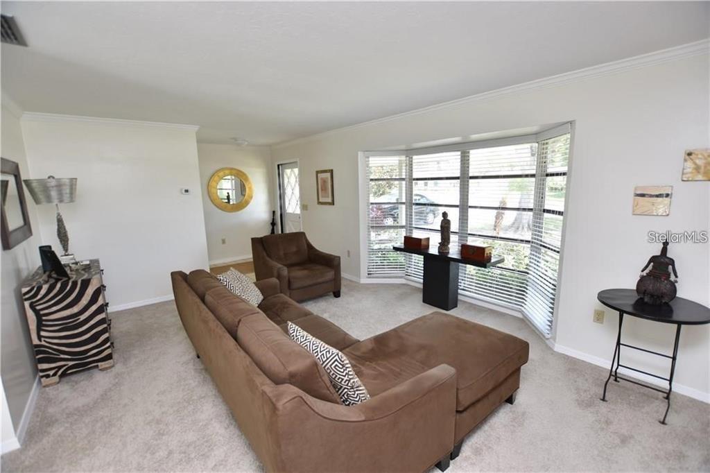 A living room features a brown sectional sofa, an armchair, and a large bay window — 3926 CALLIANDRA DRIVE, SARASOTA, FL