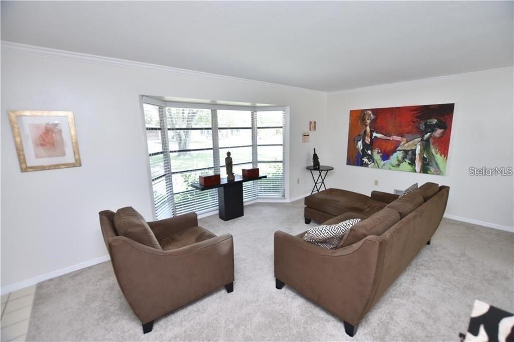A living room features a brown sectional, an armchair, and a large bay window — 3926 CALLIANDRA DRIVE, SARASOTA, FL