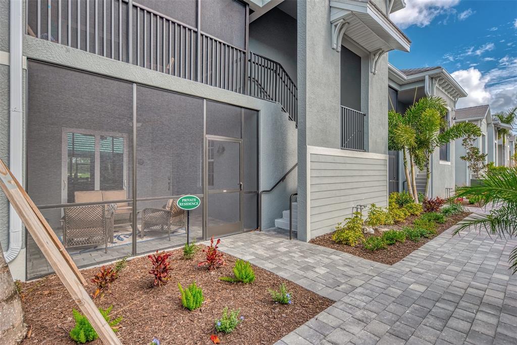 A ground-floor screened-in patio with outdoor furniture sits beside a paved walkway and landscaping — 12440 WELLEN GOLF STREET UNIT 107, VENICE, FL
