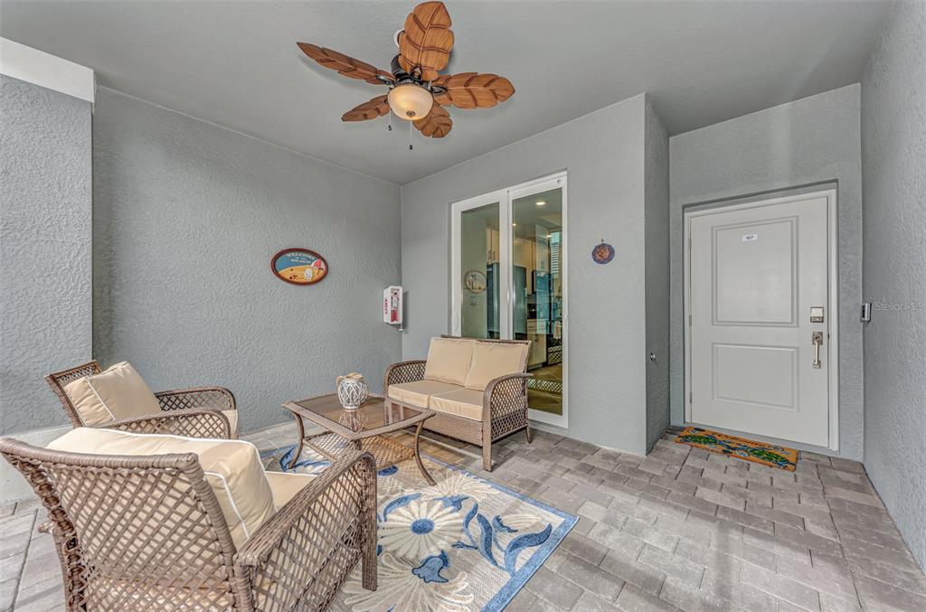 A covered patio features wicker furniture, a ceiling fan, and a glass door entrance — 12440 WELLEN GOLF STREET UNIT 107, VENICE, FL