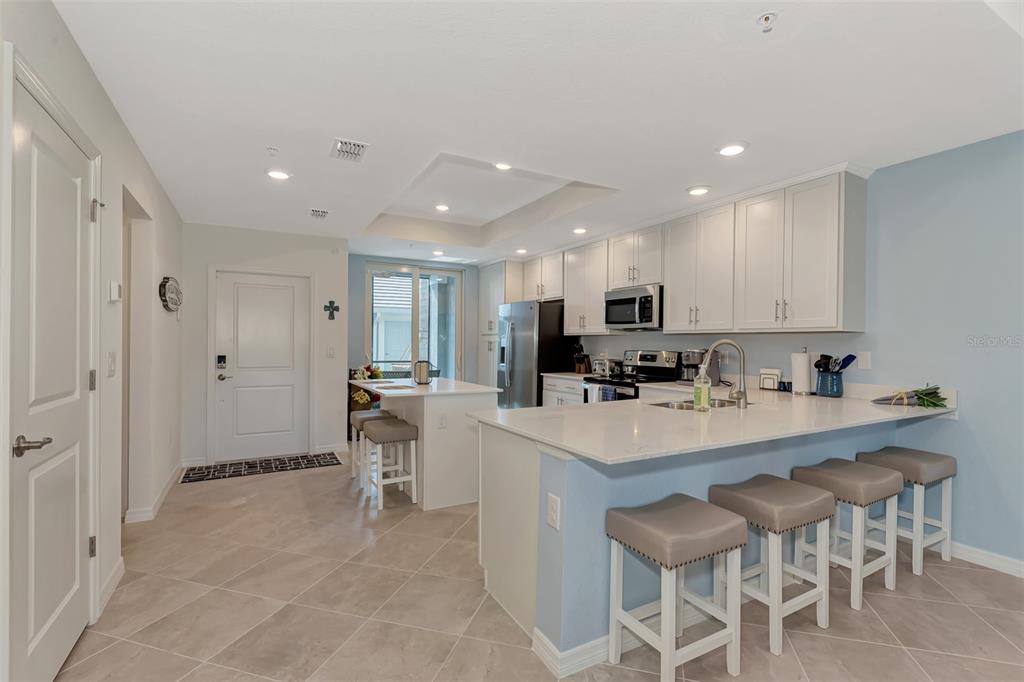 A modern kitchen features white cabinetry, quartz countertops, a breakfast bar, and light tile flooring — 12440 WELLEN GOLF STREET UNIT 107, VENICE, FL