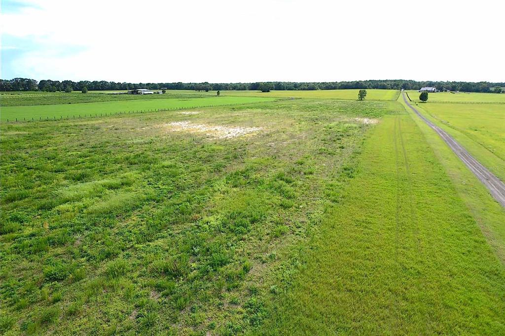 An aerial view shows a paved road running alongside a grassy field and dense trees — 00 SW 210 AVENUE, DUNNELLON, FL