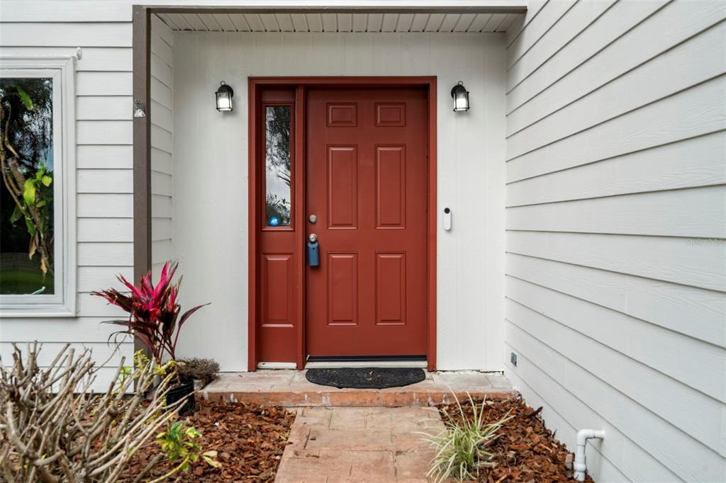 A red front door with a side light is centered on a white-sided house exterior — 15839 POWERLINE ROAD, DADE CITY, FL