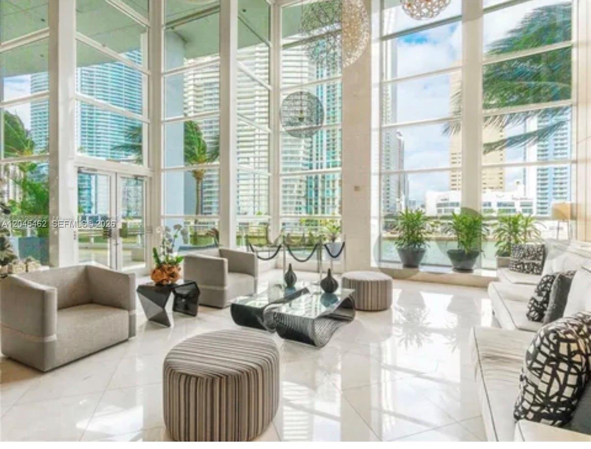 A bright, high-ceilinged living area with floor-to-ceiling windows, white tile floors, and modern furniture — 901 Brickell Key Blvd # 702, Miami FL 33131, MIAMI, FL