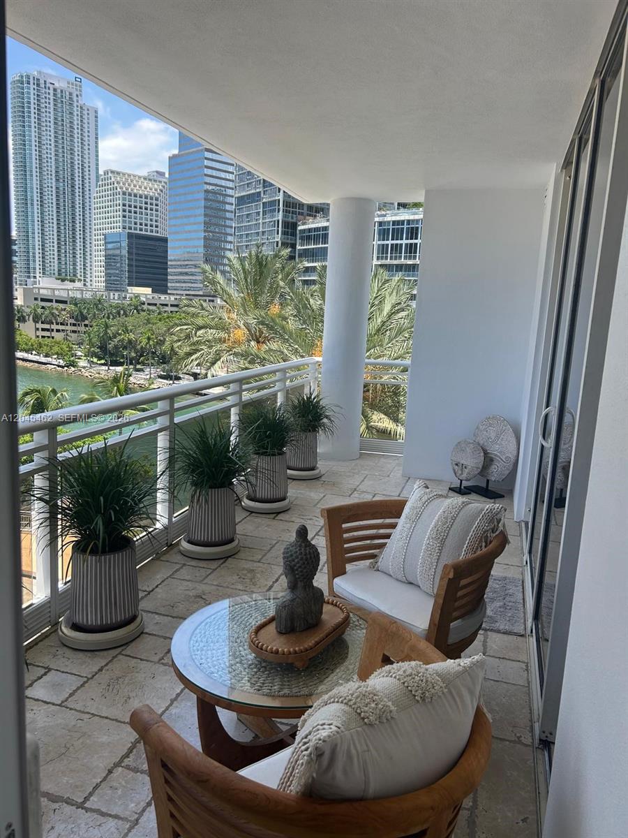 A balcony with stone flooring, two wooden chairs, a glass table, and city skyline views — 901 Brickell Key Blvd # 702, Miami FL 33131, MIAMI, FL