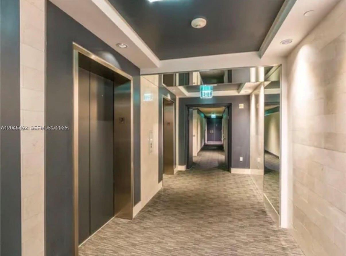 A hallway features an elevator, mirrored walls, recessed lighting, and a carpeted floor — 901 Brickell Key Blvd # 702, Miami FL 33131, MIAMI, FL