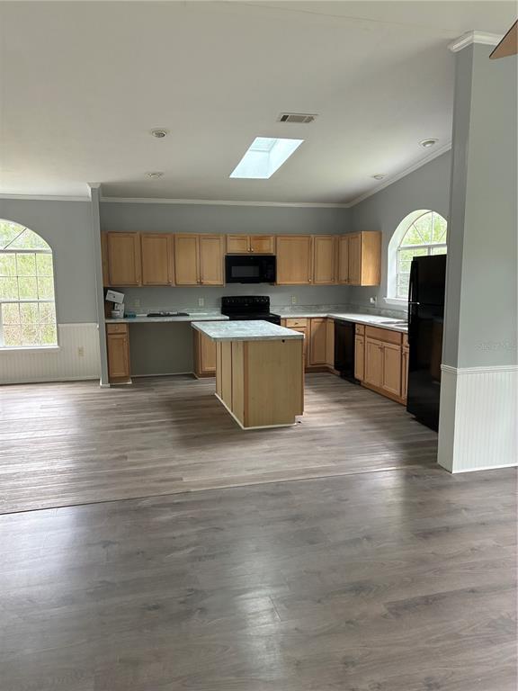 A kitchen with light wood cabinets, a central island, and black appliances on wood flooring — 3150 W CR 2006, BUNNELL, FL