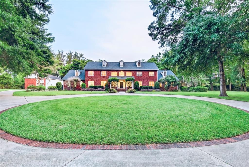A long concrete driveway leads through a tree-lined lawn to a two-story brick house — 4940 E FORT KING STREET, OCALA, FL