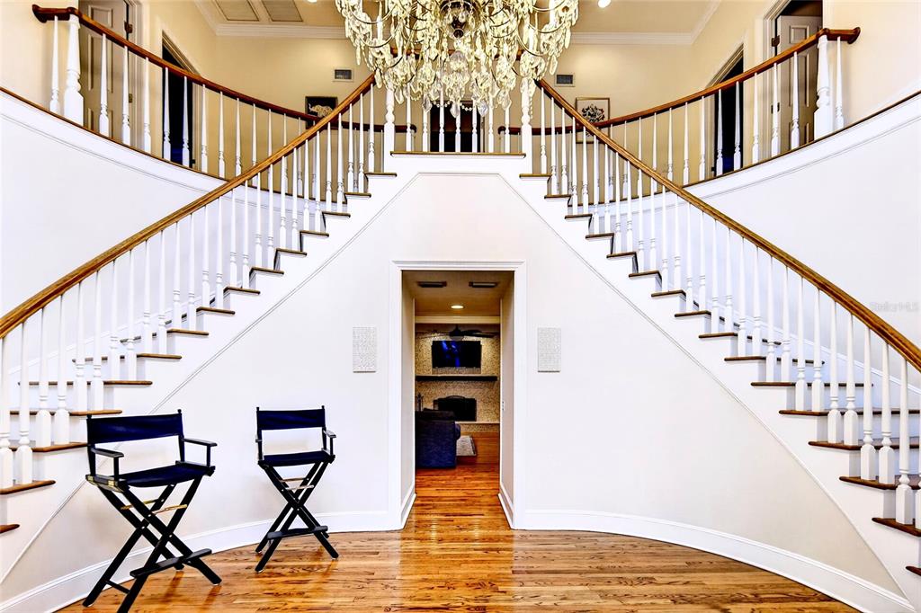 A grand foyer features a dual staircase, hardwood floors, and a central crystal chandelier — 4940 E FORT KING STREET, OCALA, FL