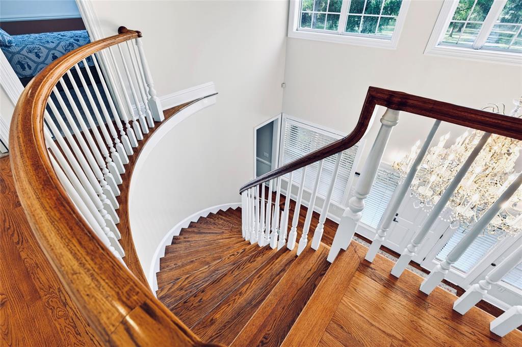 A curved wooden staircase with white balusters overlooks a foyer with a crystal chandelier — 4940 E FORT KING STREET, OCALA, FL