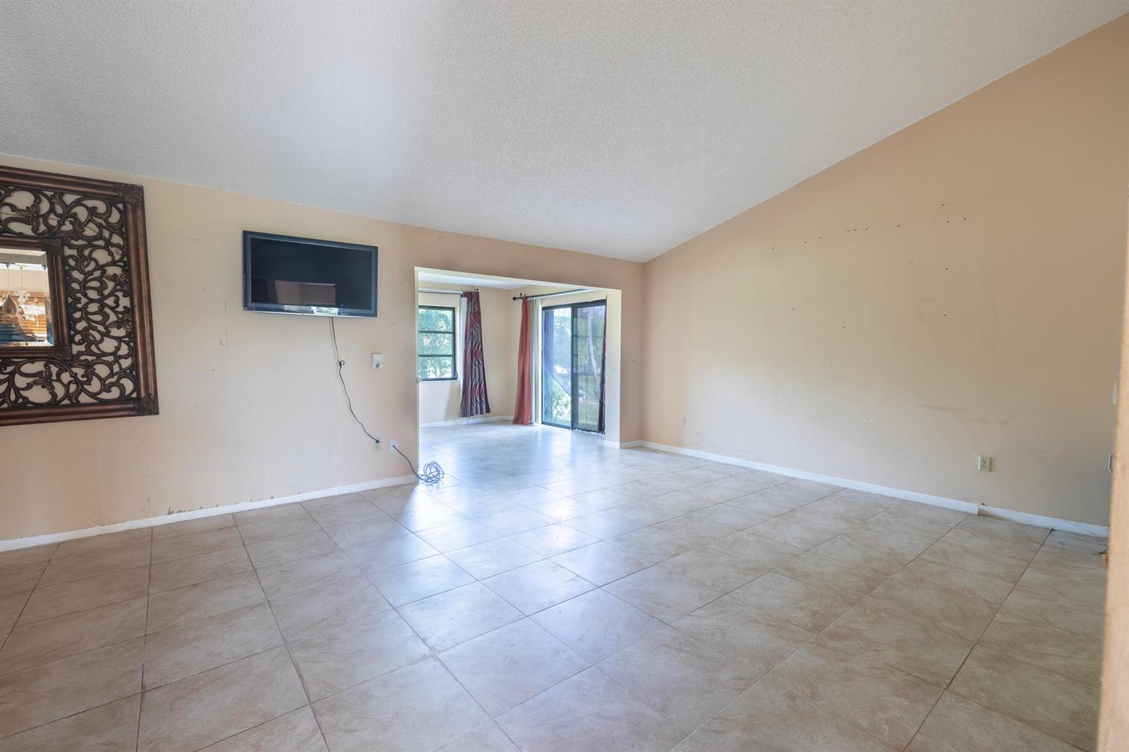 An empty living room features beige walls, tile flooring, a wall-mounted television, and sliding doors — 6149 Olivewood Circle, FL 33463, FL