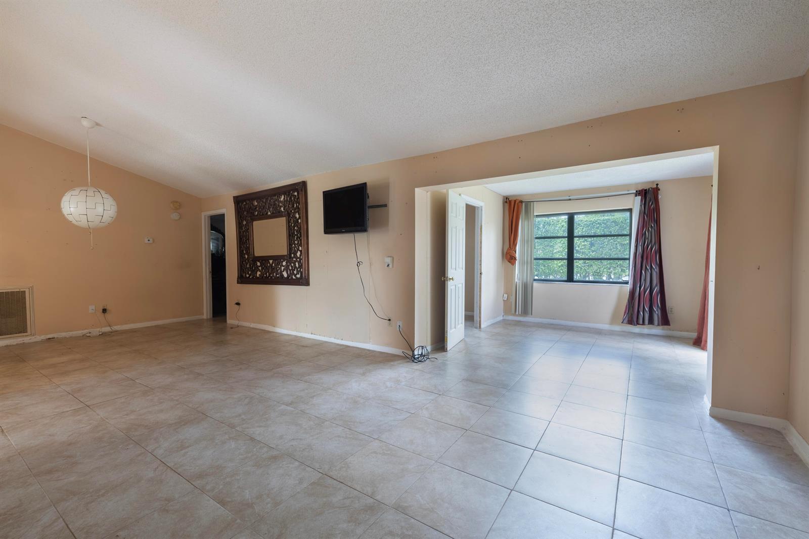 An empty living room with beige walls, tile flooring, a mounted television, and a pendant light — 6149 Olivewood Circle, FL 33463, FL