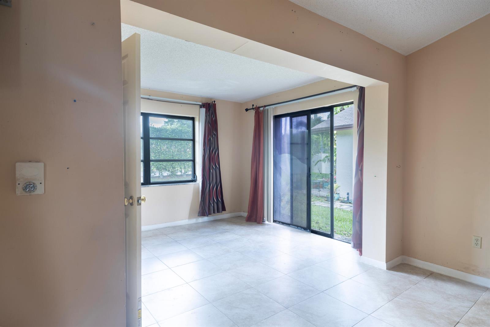 An empty room with tile flooring, a window, and sliding glass doors leading outside — 6149 Olivewood Circle, FL 33463, FL