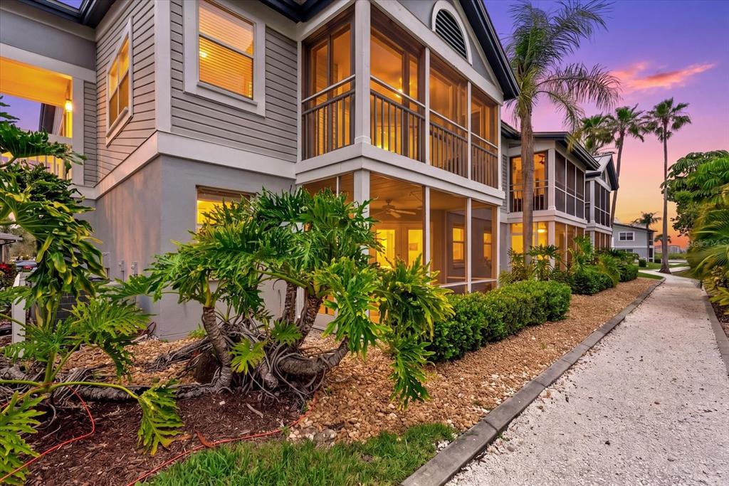 Exterior view of a multi-story building with screened balconies, landscaping, and a gravel walkway — 1332 SIESTA BAYSIDE DRIVE UNIT 1332C, SARASOTA, FL