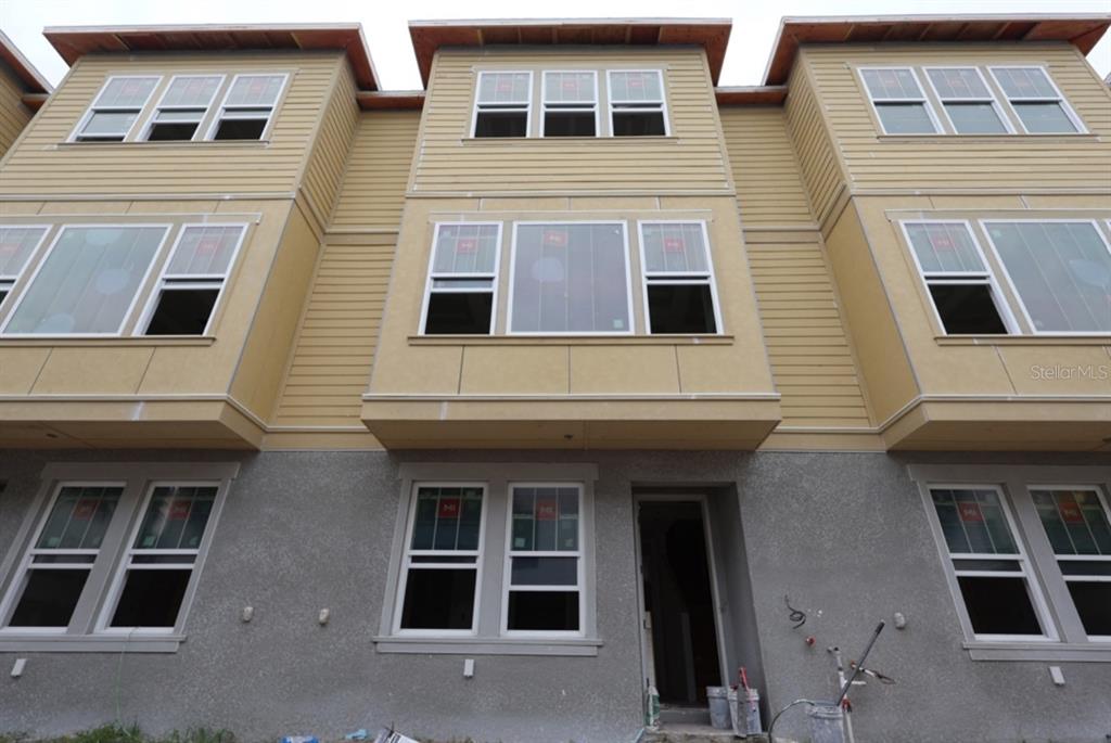 A low-angle exterior view of a three-story townhouse under construction with tan siding and stucco — 450 31ST WAY N, ST PETERSBURG, FL