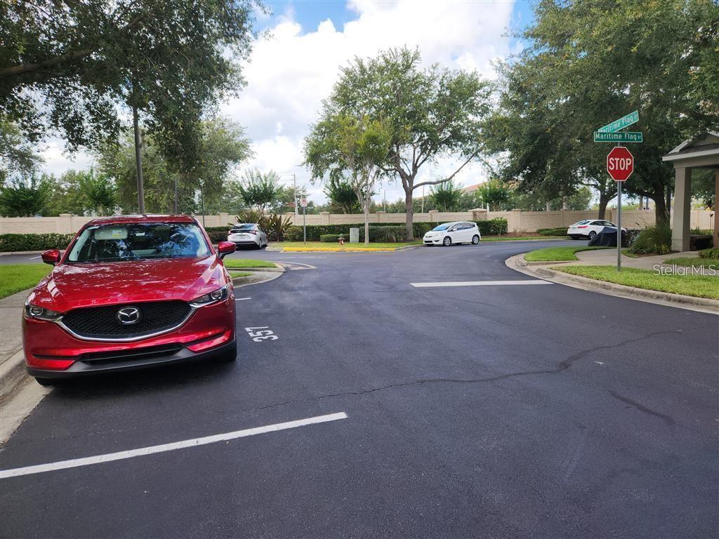 A red car is parked in a paved lot near a stop sign and trees — 8256 MARITIME FLAG STREET UNIT 1706, WINDERMERE, FL