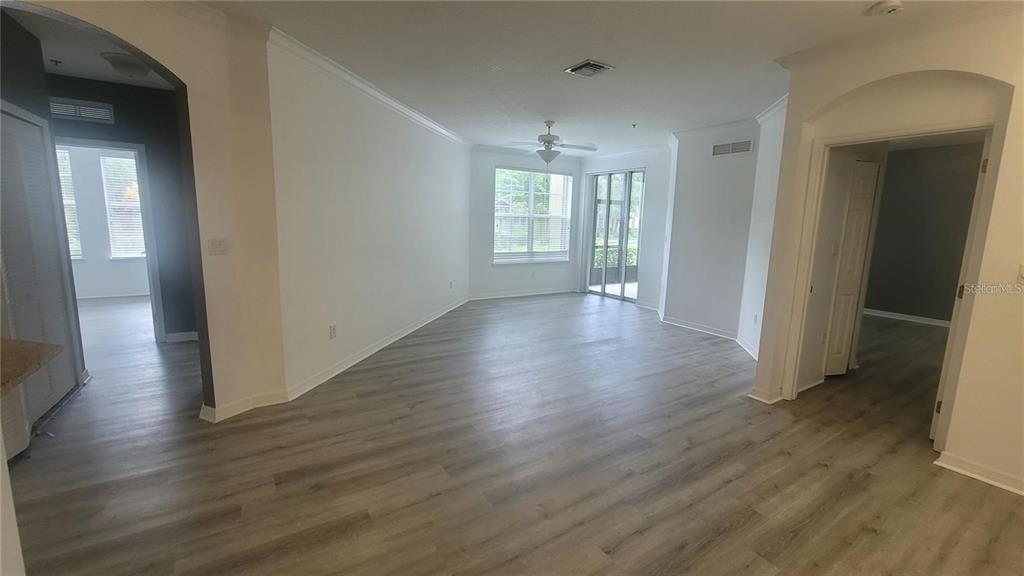 An empty living room features light wood-look flooring, white walls, a ceiling fan, and windows — 8256 MARITIME FLAG STREET UNIT 1706, WINDERMERE, FL
