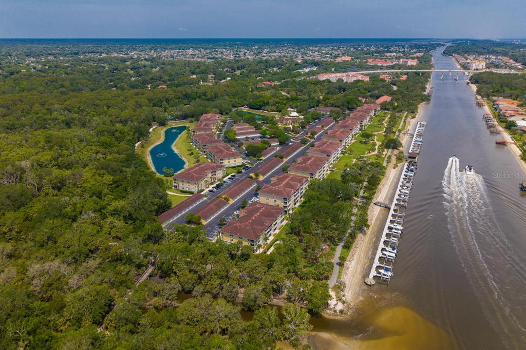 An aerial view shows a multi-building apartment complex situated next to a canal and forest — 600 CANOPY WALK LANE UNIT 634, PALM COAST, FL
