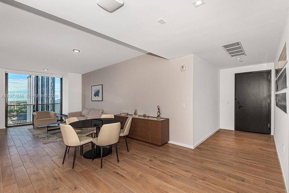 A modern living and dining area features wood flooring, floor-to-ceiling windows, and a black door — 398 NE 5th St # 2418, Miami FL 33132, MIAMI, FL