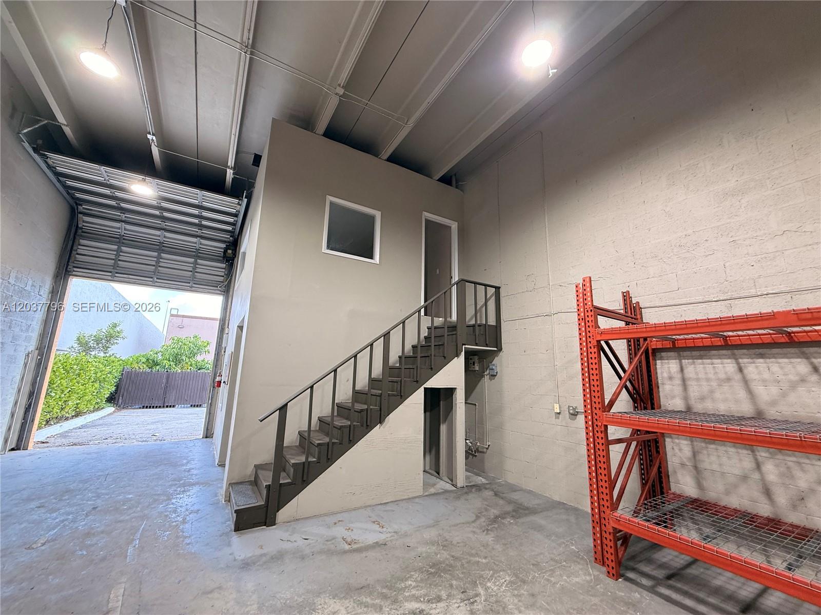 A warehouse interior features a concrete floor, a metal staircase, and orange industrial shelving — 8060 W 23rd Ave # 8, Hialeah FL 33016, HIALEAH, FL