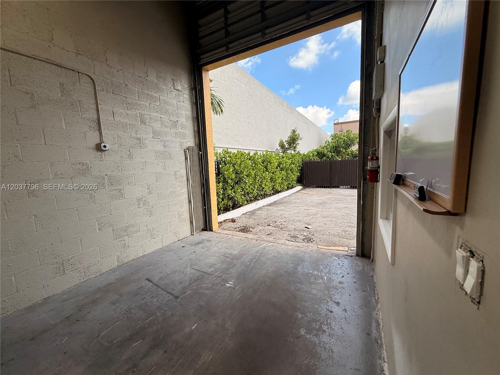 An open roll-up door leads from a concrete-floored room to an outdoor paved area — 8060 W 23rd Ave # 8, Hialeah FL 33016, HIALEAH, FL