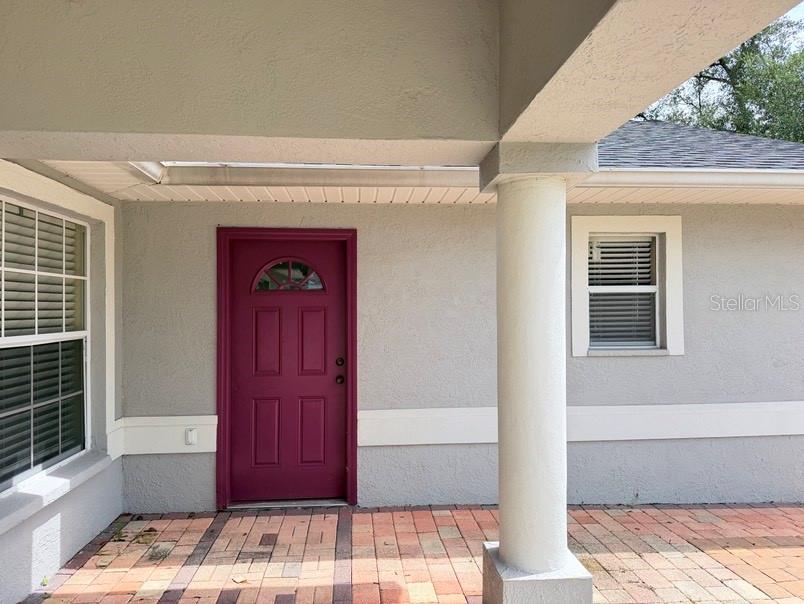 A covered porch features a magenta front door, a white column, and brick flooring — 12721 N OLA AVENUE, TAMPA, FL