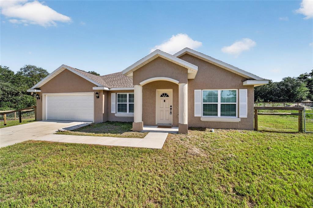 A single-story tan house with a two-car garage, white trim, and a front porch — 22081 SW PINE BLUFFS ROAD, DUNNELLON, FL