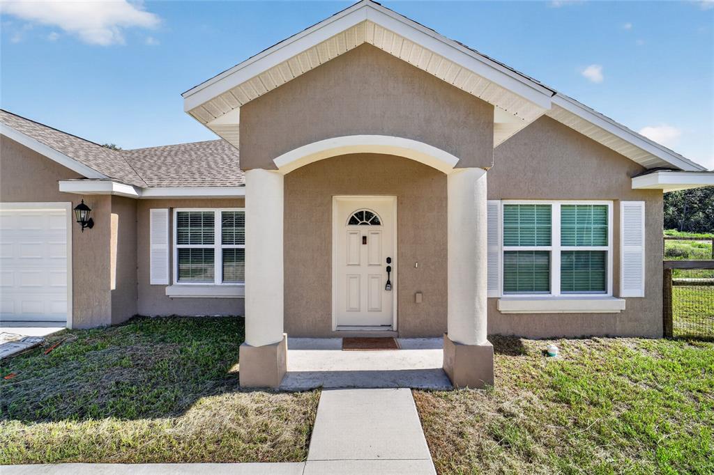 A tan stucco house features a covered entryway with two white columns and a front door — 22081 SW PINE BLUFFS ROAD, DUNNELLON, FL