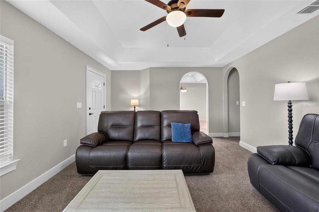 A living room features a brown leather sofa, a coffee table, and a ceiling fan — 22081 SW PINE BLUFFS ROAD, DUNNELLON, FL