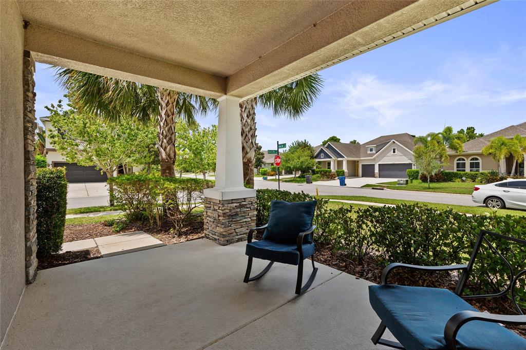 A covered concrete front porch features stone-based columns, two blue rocking chairs, and neighborhood views — 7502 SEA LILLY COURT, APOLLO BEACH, FL