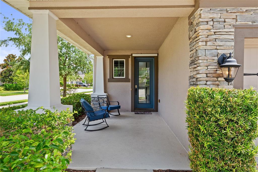 A covered front porch features a blue door, two rocking chairs, and stone siding — 7502 SEA LILLY COURT, APOLLO BEACH, FL