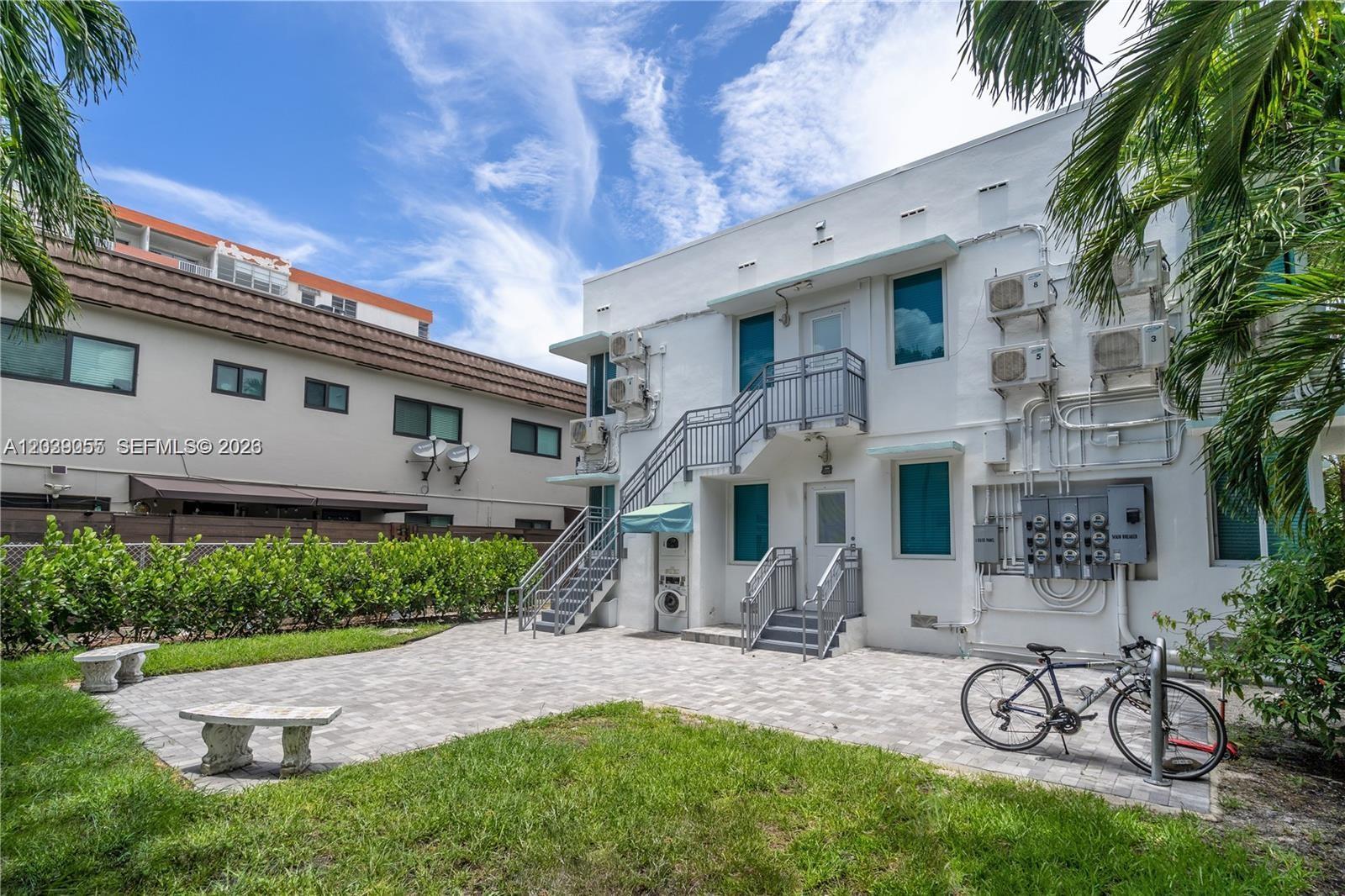 A white two-story apartment building features exterior staircases, a paved patio, and a bicycle — 7936 Harding Ave # 5, Miami Beach FL 33141, MIAMI BEACH, FL