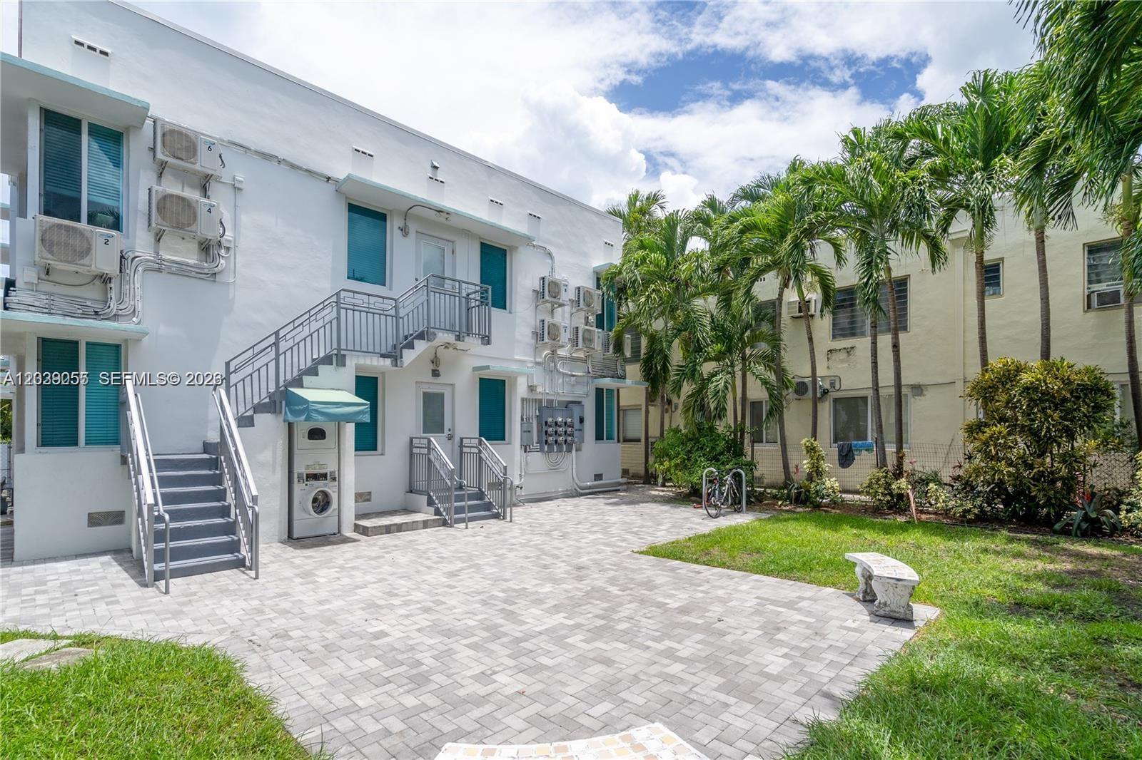 A paved courtyard sits between two multi-story apartment buildings with exterior staircases and palm trees — 7936 Harding Ave # 5, Miami Beach FL 33141, MIAMI BEACH, FL