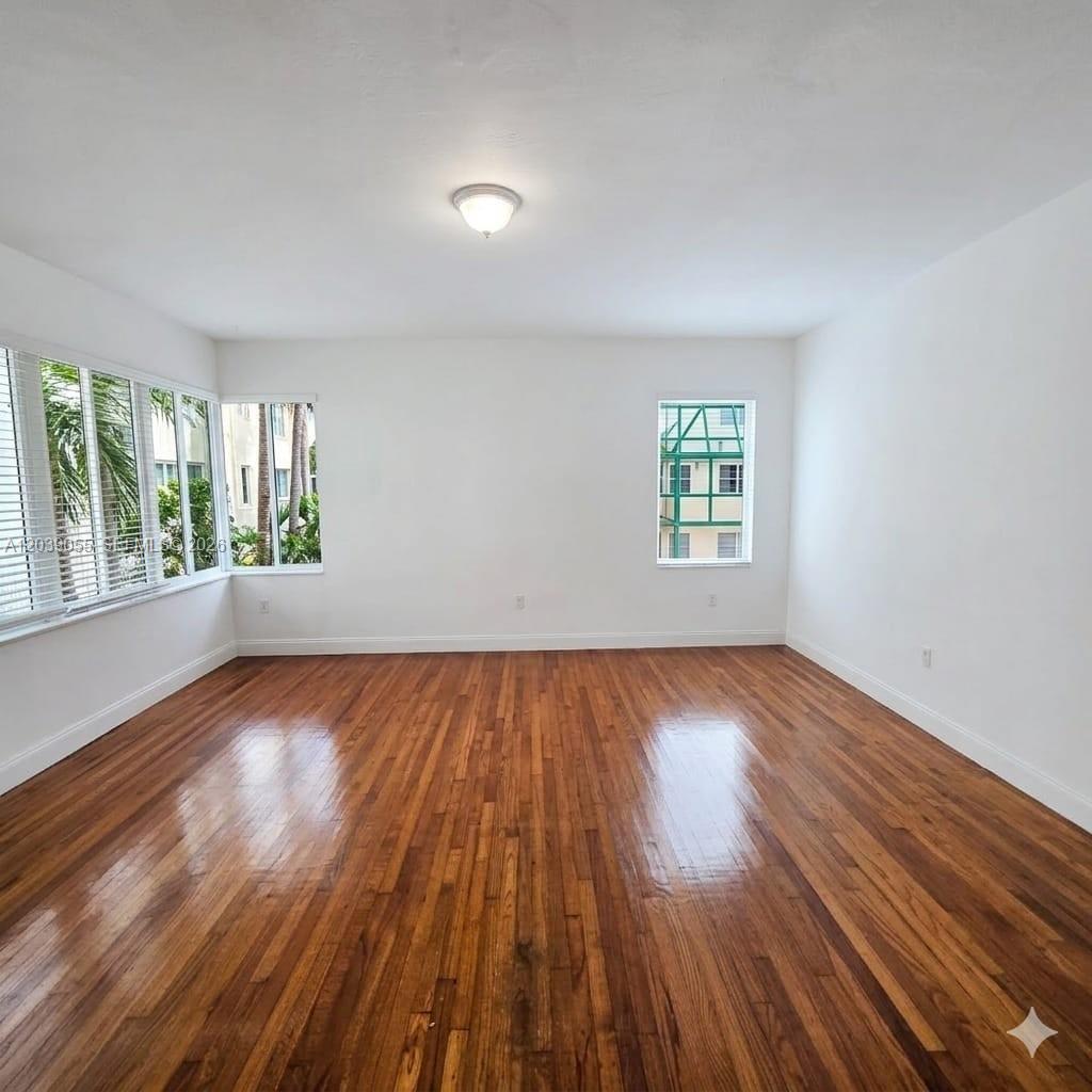 An empty room with hardwood floors, white walls, and multiple windows — 7936 Harding Ave # 5, Miami Beach FL 33141, MIAMI BEACH, FL